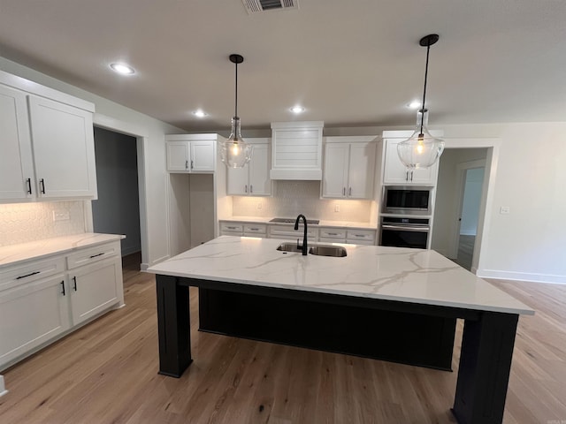 kitchen featuring light wood finished floors, custom exhaust hood, stainless steel appliances, white cabinetry, and a sink