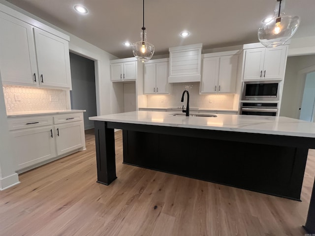 kitchen with appliances with stainless steel finishes, white cabinets, a sink, and light wood-style flooring