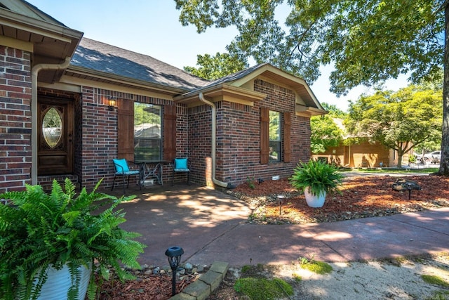 exterior space with brick siding and roof with shingles