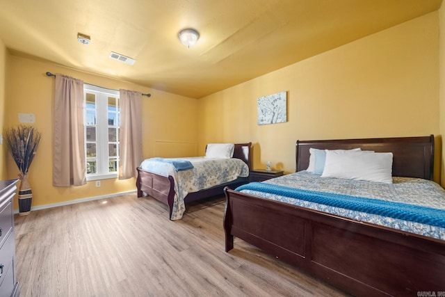 bedroom with baseboards, visible vents, and wood finished floors