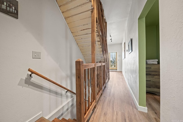 hallway featuring a textured wall, baseboards, wood finished floors, and an upstairs landing