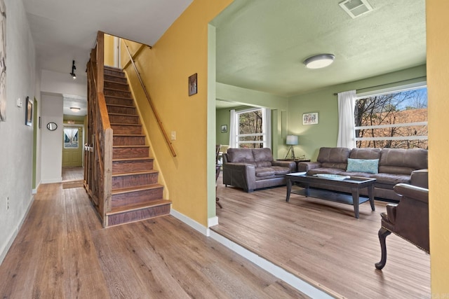 living room with stairs, wood finished floors, visible vents, and baseboards