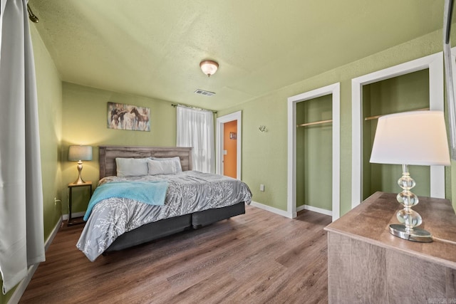 bedroom with baseboards, a textured ceiling, visible vents, and wood finished floors