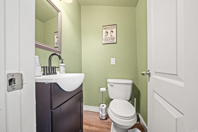 half bathroom featuring toilet, baseboards, wood finished floors, and vanity