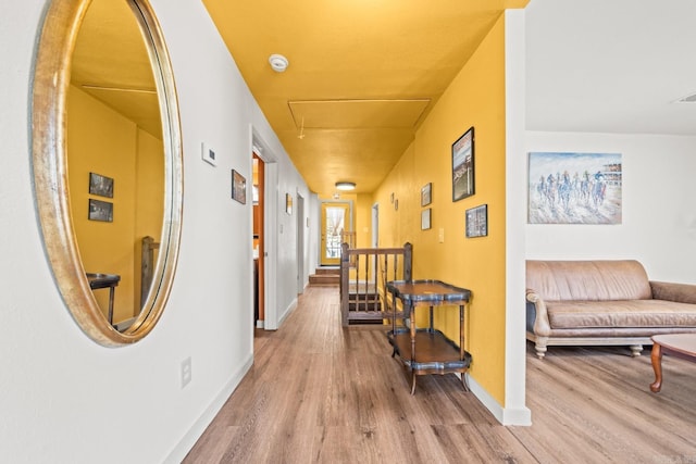 corridor featuring attic access, visible vents, baseboards, and wood finished floors