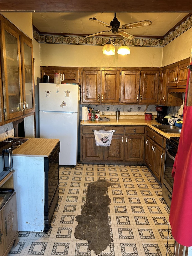 kitchen featuring ceiling fan, stainless steel range with gas stovetop, freestanding refrigerator, light countertops, and a sink