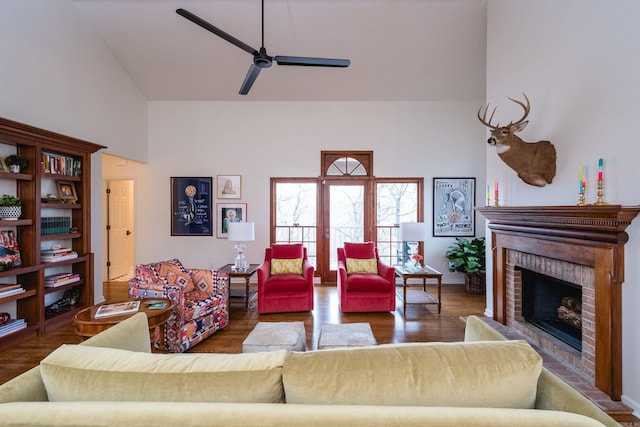 living area featuring ceiling fan, a fireplace, a towering ceiling, and wood finished floors