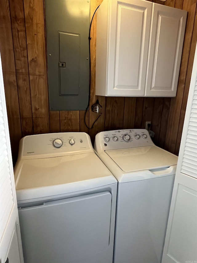 laundry room featuring cabinet space, electric panel, wood walls, and independent washer and dryer