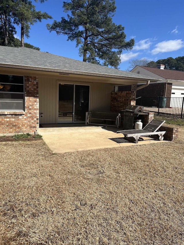 back of property with brick siding, roof with shingles, and a patio area