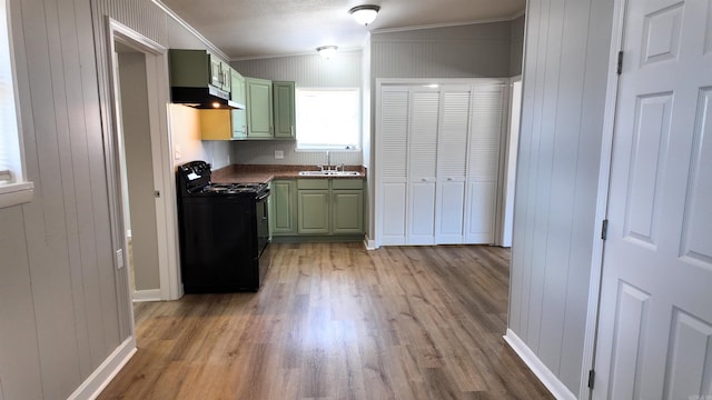 kitchen featuring black gas range, light wood-style flooring, ornamental molding, green cabinets, and a sink