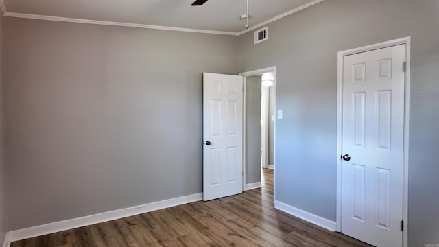 unfurnished bedroom featuring wood finished floors, a ceiling fan, visible vents, baseboards, and crown molding