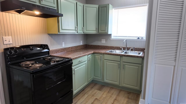 kitchen featuring light wood-style floors, black / electric stove, under cabinet range hood, green cabinets, and a sink