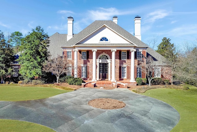 view of front facade featuring brick siding, a chimney, and a front lawn