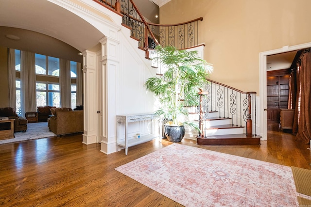 foyer with high vaulted ceiling, arched walkways, stairs, and wood finished floors