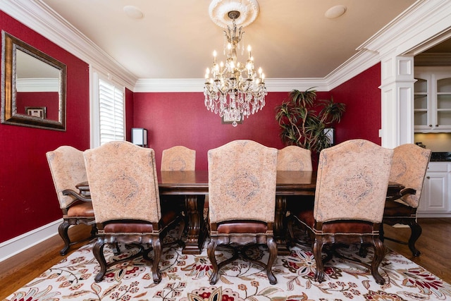 dining room with a notable chandelier, ornamental molding, an accent wall, wood finished floors, and baseboards