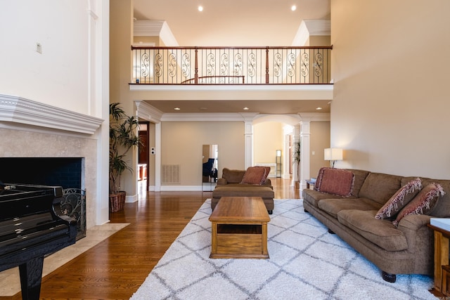 living area featuring decorative columns, baseboards, a premium fireplace, ornamental molding, and wood finished floors