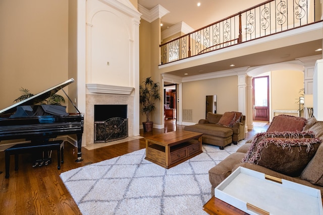 living area featuring ornamental molding, decorative columns, a fireplace with flush hearth, and wood finished floors