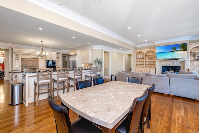 dining room with light wood-type flooring, a fireplace, a chandelier, and recessed lighting