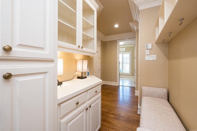 interior space with dark wood-style floors, light countertops, ornamental molding, glass insert cabinets, and white cabinetry