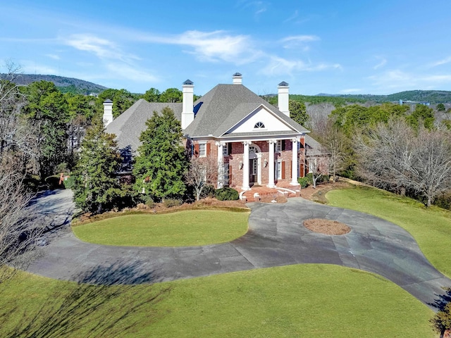 greek revival inspired property with a front yard, a chimney, and brick siding