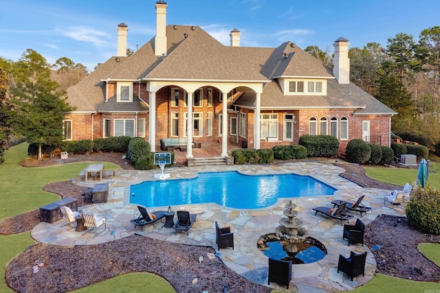 rear view of property featuring a fire pit, an outdoor pool, roof with shingles, a patio area, and brick siding