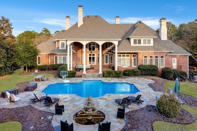 rear view of property with brick siding, a shingled roof, an outdoor fire pit, a patio area, and an outdoor pool