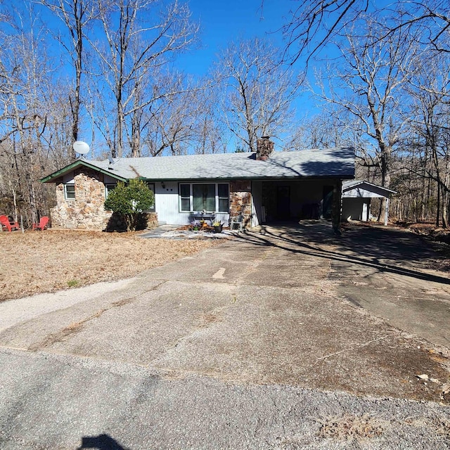 view of front of house featuring driveway, stone siding, and a chimney