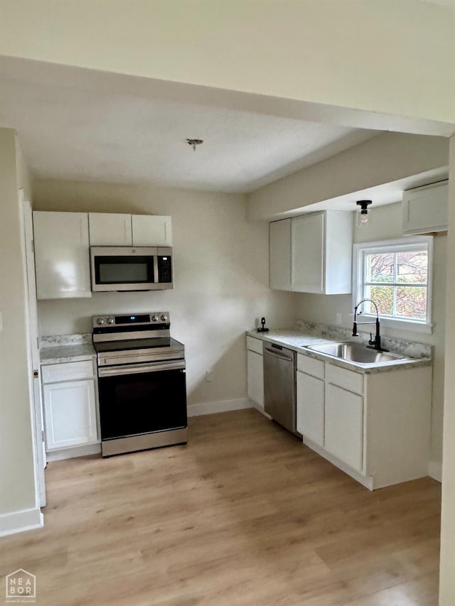 kitchen with white cabinets, light wood-style flooring, stainless steel appliances, and a sink