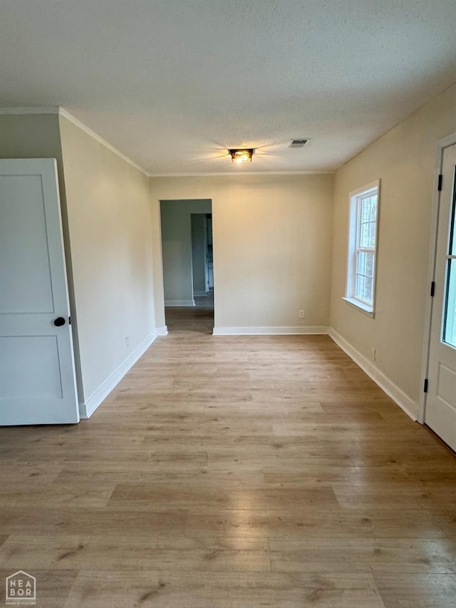 empty room featuring a textured ceiling, visible vents, baseboards, ornamental molding, and light wood finished floors