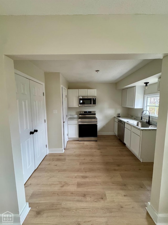 kitchen with stainless steel appliances, a sink, white cabinetry, and light wood-style floors