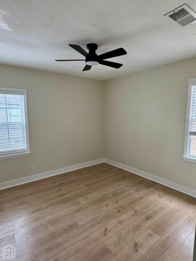 empty room with visible vents, baseboards, light wood-style flooring, ceiling fan, and a textured ceiling