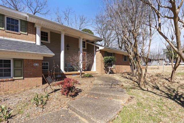 view of front facade with a shingled roof, crawl space, brick siding, and a porch