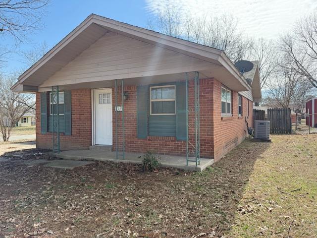 bungalow with brick siding, a porch, fence, and central air condition unit