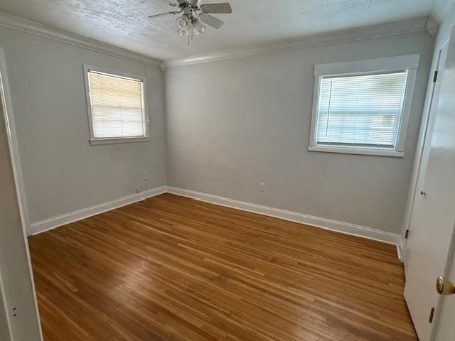 spare room featuring a textured ceiling, ornamental molding, wood finished floors, and a wealth of natural light