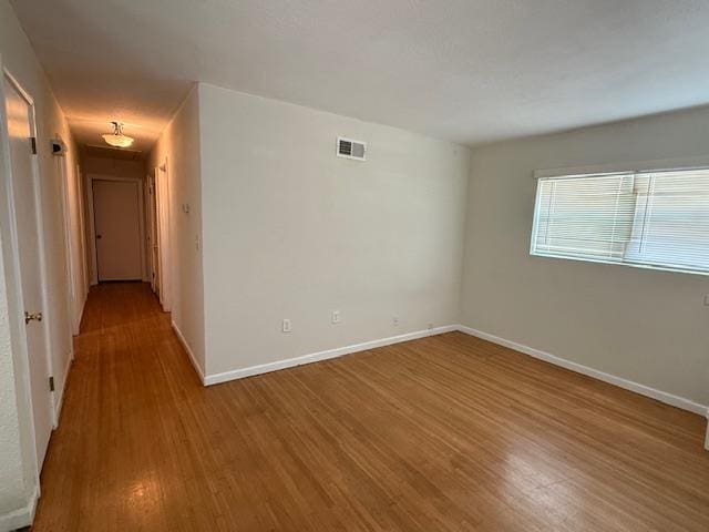 spare room featuring baseboards, visible vents, and wood finished floors