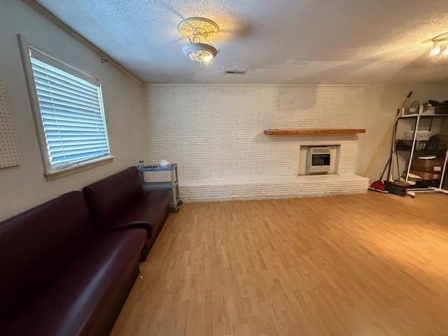 living area featuring a brick fireplace, brick wall, a textured ceiling, and wood finished floors