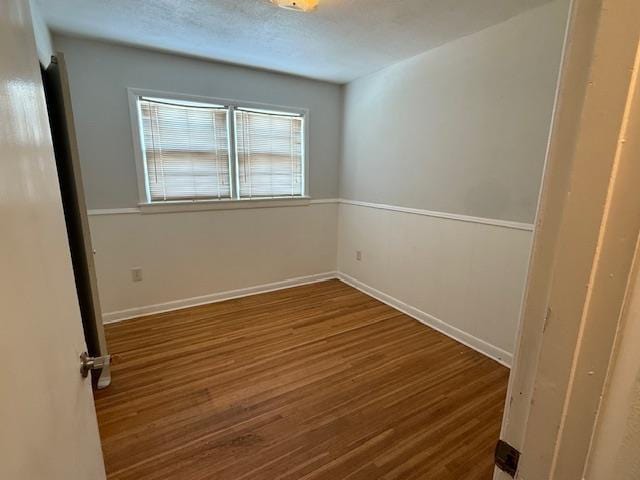 empty room featuring a textured ceiling, wood finished floors, and baseboards