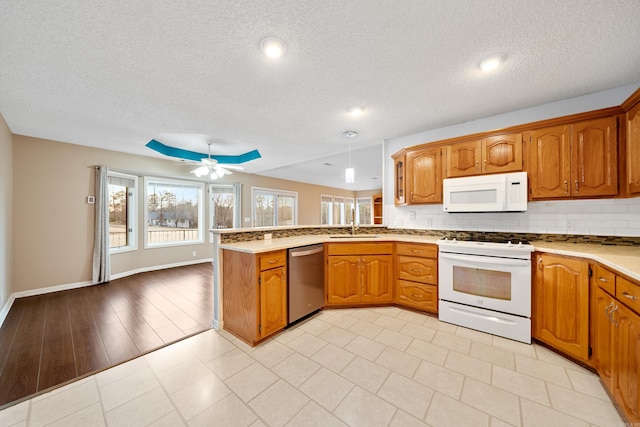 kitchen featuring white appliances, brown cabinets, a peninsula, and backsplash