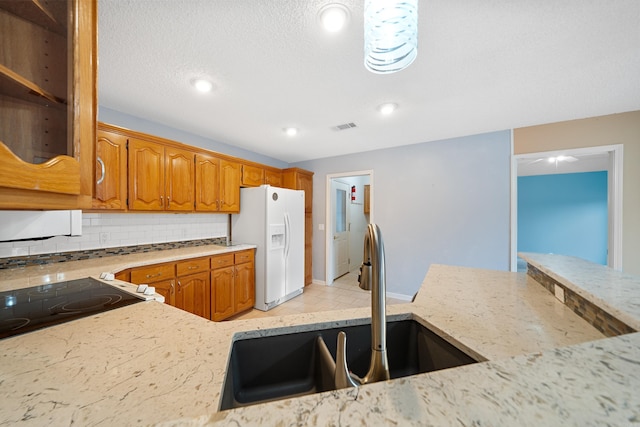 kitchen featuring tasteful backsplash, white refrigerator with ice dispenser, visible vents, brown cabinetry, and a sink