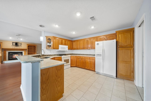 kitchen featuring a ceiling fan, a glass covered fireplace, a sink, white appliances, and a peninsula