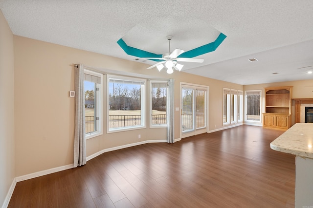 unfurnished living room featuring baseboards, dark wood finished floors, a ceiling fan, a glass covered fireplace, and a textured ceiling