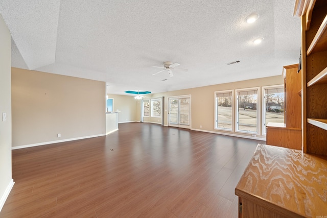 unfurnished living room featuring baseboards, visible vents, ceiling fan, dark wood-style flooring, and a textured ceiling