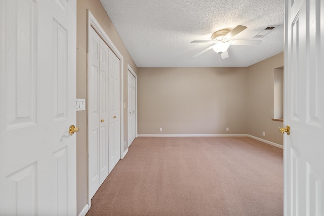 unfurnished bedroom with a textured ceiling, light carpet, visible vents, baseboards, and two closets