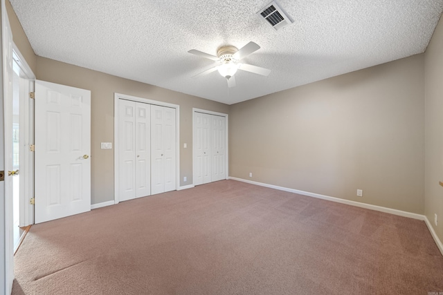 unfurnished bedroom featuring baseboards, visible vents, ceiling fan, carpet, and two closets