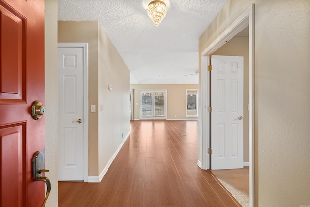 corridor with a textured ceiling, baseboards, and wood finished floors