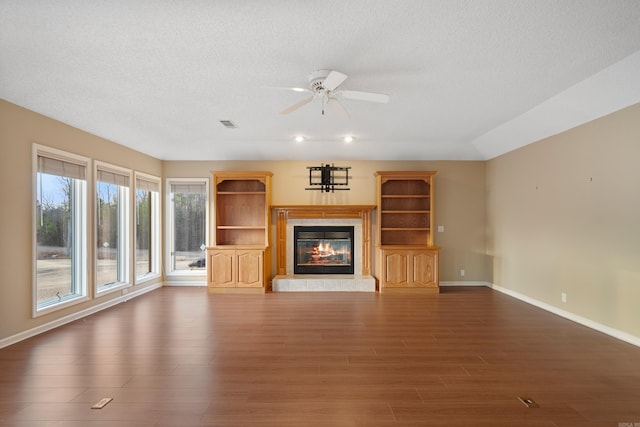 unfurnished living room featuring a glass covered fireplace, dark wood finished floors, a textured ceiling, and ceiling fan