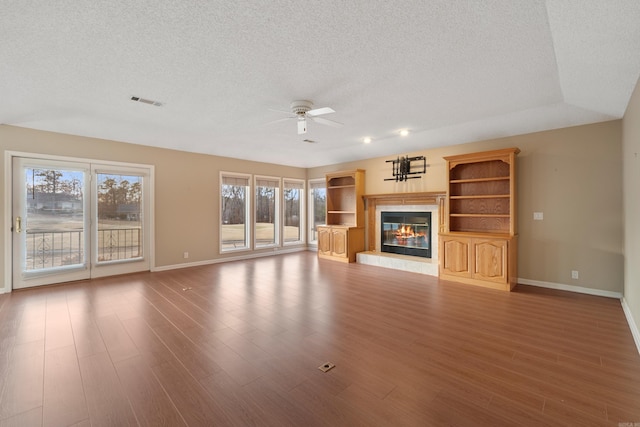 unfurnished living room featuring a textured ceiling, a fireplace, wood finished floors, a ceiling fan, and baseboards