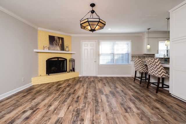 unfurnished living room with baseboards, ornamental molding, wood finished floors, a brick fireplace, and a sink