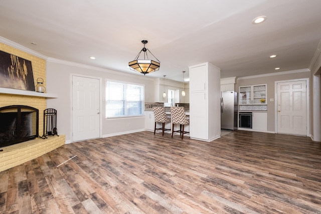 unfurnished living room featuring recessed lighting, dark wood-type flooring, baseboards, a brick fireplace, and crown molding