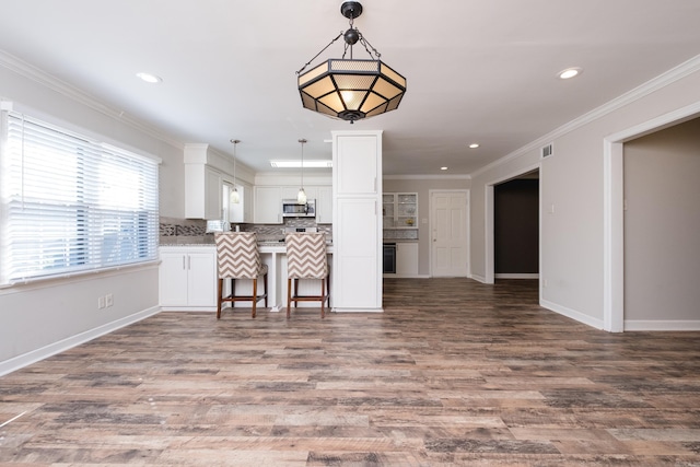 kitchen with crown molding, stainless steel microwave, decorative backsplash, open floor plan, and white cabinets